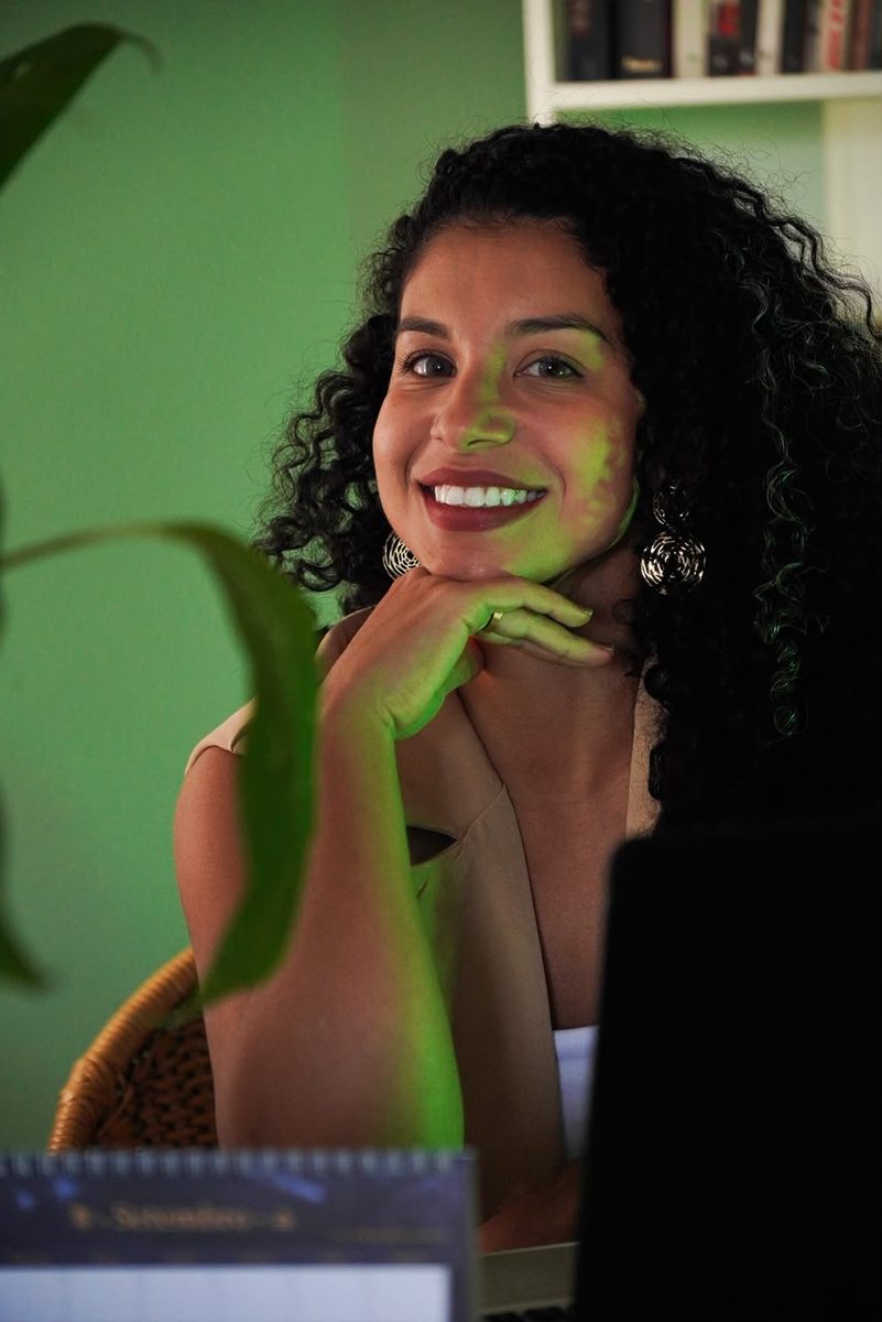 Kamilla Fidelis sorrindo no consultório, com plantas ao fundo