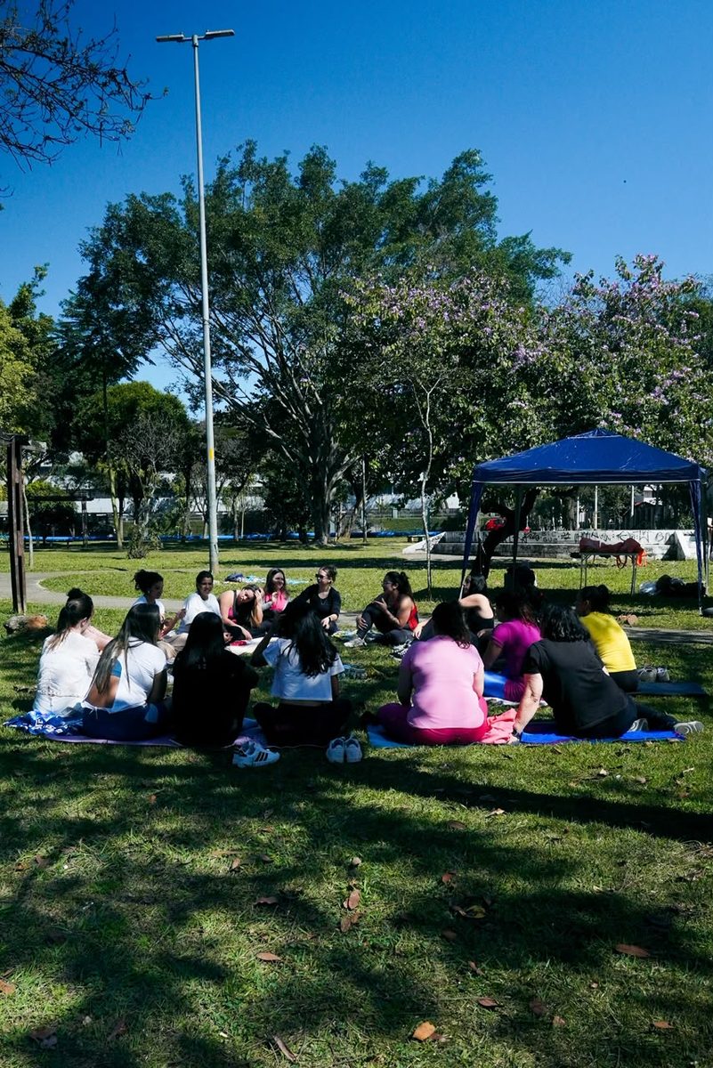 Roda de mulheres sentadas no gramado durante encontro ao ar livre